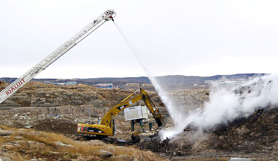 An excavator from the department of public works digs at part of the Iqaluit dump fire on Oct. 1, exposing hot embers to sprays of water from the fire engine. (PHOTO BY CHRIS WINDEYER)