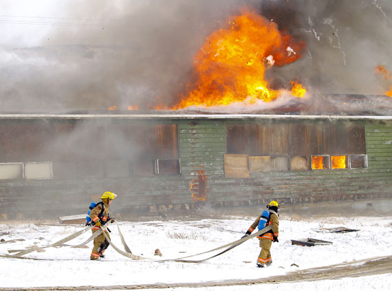 Firefighters carry hoses past the burning shell of the former Sir Martin Frobisher federal day school in Apex Oct. 4. The fire forced nearby Nanook school to close and power to the surrounding neighbourhood to be briefly shut off. (PHOTO BY CHRIS WINDEYER)
