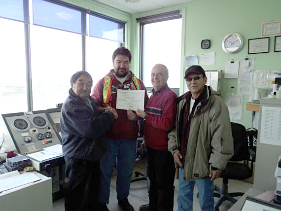 Bobby Aupaluk, centre left, was presented his observer-communicator certificate at the Puvirnituq airport Oct. 25 by ATS Services instructor Marcel Lefebvre, centre right, with Puvirnituq mayor Aisara Kenuajuak, left, and senior observer-communicator William Quara, right. Observer-communicators use aerodrome radio stations in Nunavik to transmit local weather and runway conditions to regional airline pilots. Aupaluk trained for six-weeks at a centre in Cornwall, Ontario, before completing a three-week internship in Puvirnituq. (PHOTO COURTESY OF THE KRG)