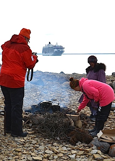 As a passenger from The World takes photos, Eva Otokiak and Mary Avalak tend to a fire Aug. 30 with The World in the background. (PHOTO BY PAUL BILLOWES/ KITIKMEOT HERITAGE SOCIETY)

