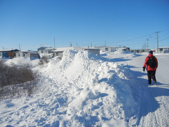 A pedestrian walks down the street edged by tall snowdrifts in Kuujjuaq. More snow than average has fallen this past winter in Kuujjuaq, Environment Canada confirms. (PHOTO BY JANE GEORGE)