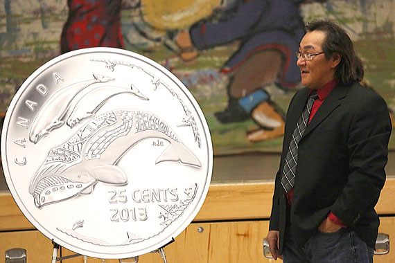 Kinngait artist Tim Pitsiulak stands beside the rendering of a new 25 cent coin that he designed for the Royal Canadian Mint and which was unveiled in Cambridge Bay Nov. 22. The new coin, which is not yet in circulation, was designed to celebrate the 100th anniversary of the Canadian Arctic Expedition, 