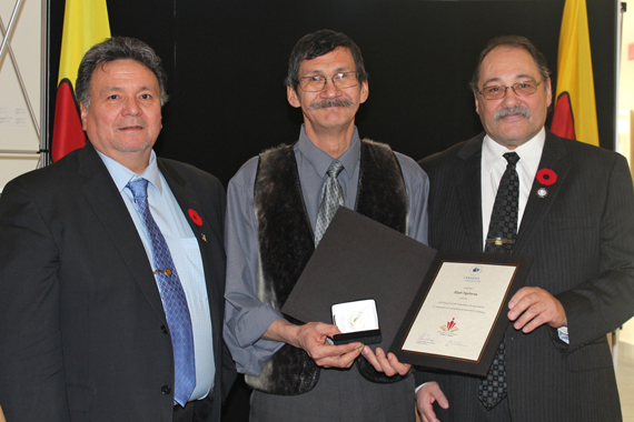 Premier Peter Taptuna, left, and Tununiq MLA Joe Enook, right, present the 2015 Council of the Federation Literacy award to Pond Inlet educator Elijah Tigullaraq Nov. 5 at the legislative assembly. Tigullaraq received the award for decades of work with Nunavut’s education department as a bilingual language consultant, teaching Inuit and non-Inuit using methods inspired by Inuit Qaujimajatuqangit. The award has been handed out to a recipient in each of the country’s provinces and territories every year since 2004. (PHOTO COURTESY OF THE GN)