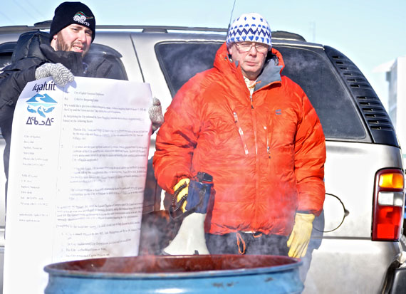 Bill Fennell, the president of the Nunavut Employees Union (right), and another member of the Public Service Alliance of Canada burn a giant copy of the letter that the City of Iqaluit attached to employee pay stubs this week. (PHOTO BY STEVE DUCHARME)
