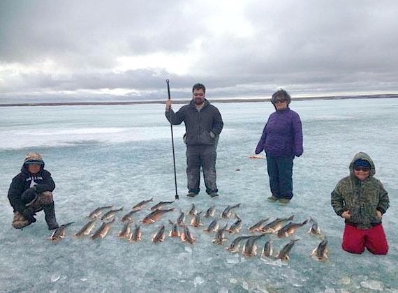 Good catch: Young fishermen and brothers Sammy Bruce, left, and Etuvik Bruce, right show off the bounty of Arctic char they pulled in outside of Coral Harbour June 20. The boys' proud father Dennis Bruce and their grandmother Pasha Bruce look on in the background. (PHOTO BY GERALDINE BRUCE) 
