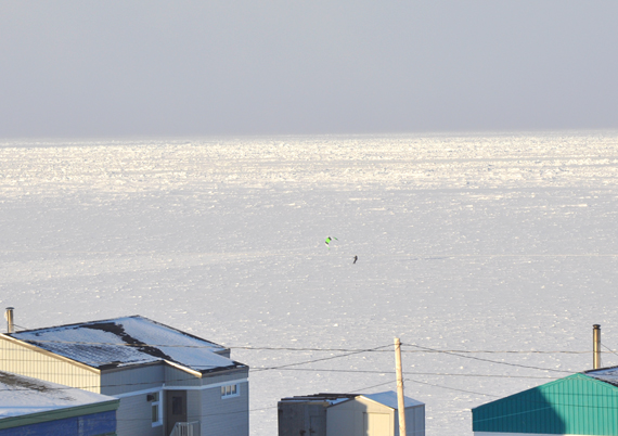 Spot the kite-skier, with a green and black sail, catching wind and some bright sunshine on the frozen shore of Ivujivik Feb. 21. Nunavik's northernmost village is located at the northwest tip of the region, where Hudson Strait meets Hudson Bay. (PHOTO BY SARAH ROGERS) 