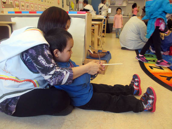 ECE graduate Charlotte Maktar teaches preschooler Mason Angnetsiak how to use a bone bow and arrow.