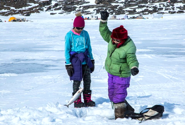Olayuk Kigutikarjuk of Arctic bay snags an Arctic char as Hillary Kines looks on during an annual May long weekend fishing derby at Ikpikituarjuk, about 165 km by snowmobile from Arctic Bay. Dozens of families gathered in more than 50 tents set up on the lake this year and for good reason—prizes were generous. Hannah Akikulu won a snowmobile this year at the Ikpikituarjuk derby with a 29.8-inch char and Ryan Willie won $5,000 for the Arctic Bay sculpin derby, held near town, with a 18.4-inch fish. There were also prizes for those 15 years old and under: Lindsay Kalluk won $750 for her 18-inch sculpin and Cameron Arnauyumayuq won $750 at Ikpikituarjuk with a 27.1-inch char. (PHOTO BY CLARE KINES)