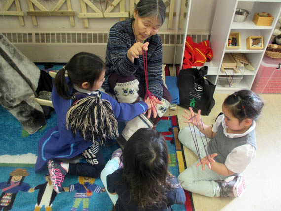 Early childhood educator and elder Ruth Sangoya shows Piruvik preschoolers Lily Koonoo, Naya Elverum and Hazel Sangoya how to play traditional string games. (PHOTO BY TESSA LOCHHEAD)