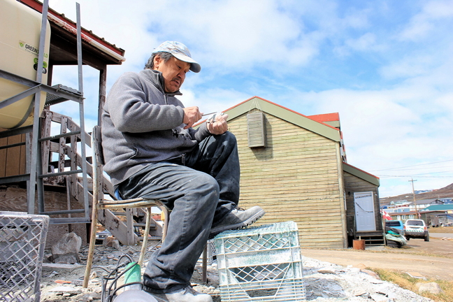 Tommy Takpanie Jr. enjoys warm weather in Nunavut's capital June 13 to carve a polar bear from serpentine soapstone. It takes about an hour to carve a small polar bear, he says and he can usually sell it for $80 to $100. 