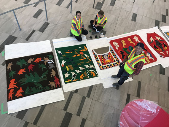 Winnipeg Art Gallery curator Andrew Kear, front, along with Government of Nunavut art curator Krista Zawadski, left, and Serge Saurette prepare to hang five large-scale, Nunavut-made wall hangings inside the new Iqaluit International Airport, which celebrated its official grand opening this week, on Sept. 13. The wall hangings are among 7,300 pieces of art from the Government of Nunavut's Fine Arts Collection currently stored in trust at the Winnipeg Art Gallery. The WAG helped to transfer and install dozens of pieces of art at the new 9,000 square foot airport, including 58 sculptures made by Inuit artists. (PHOTO COURTESY OF WAG) 
