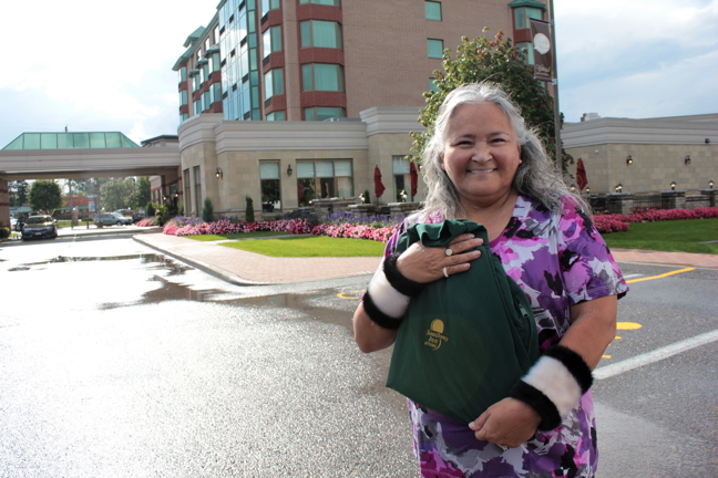 Former Iqaluit mayor, and frequent Southway Inn patron, holds up her Southway Inn shirt in front of the old hotel, now a retirement residence at Bank Street and Hunt Club Road. 