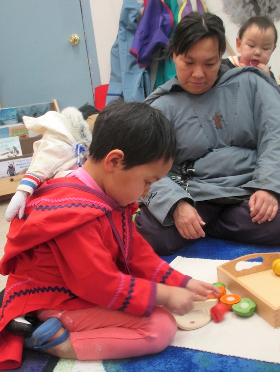 A young girl wearing an amautik cuts up a wooden apple at the Ilisaqsivik preschool, in an activity that builds co-ordination and confidence.
