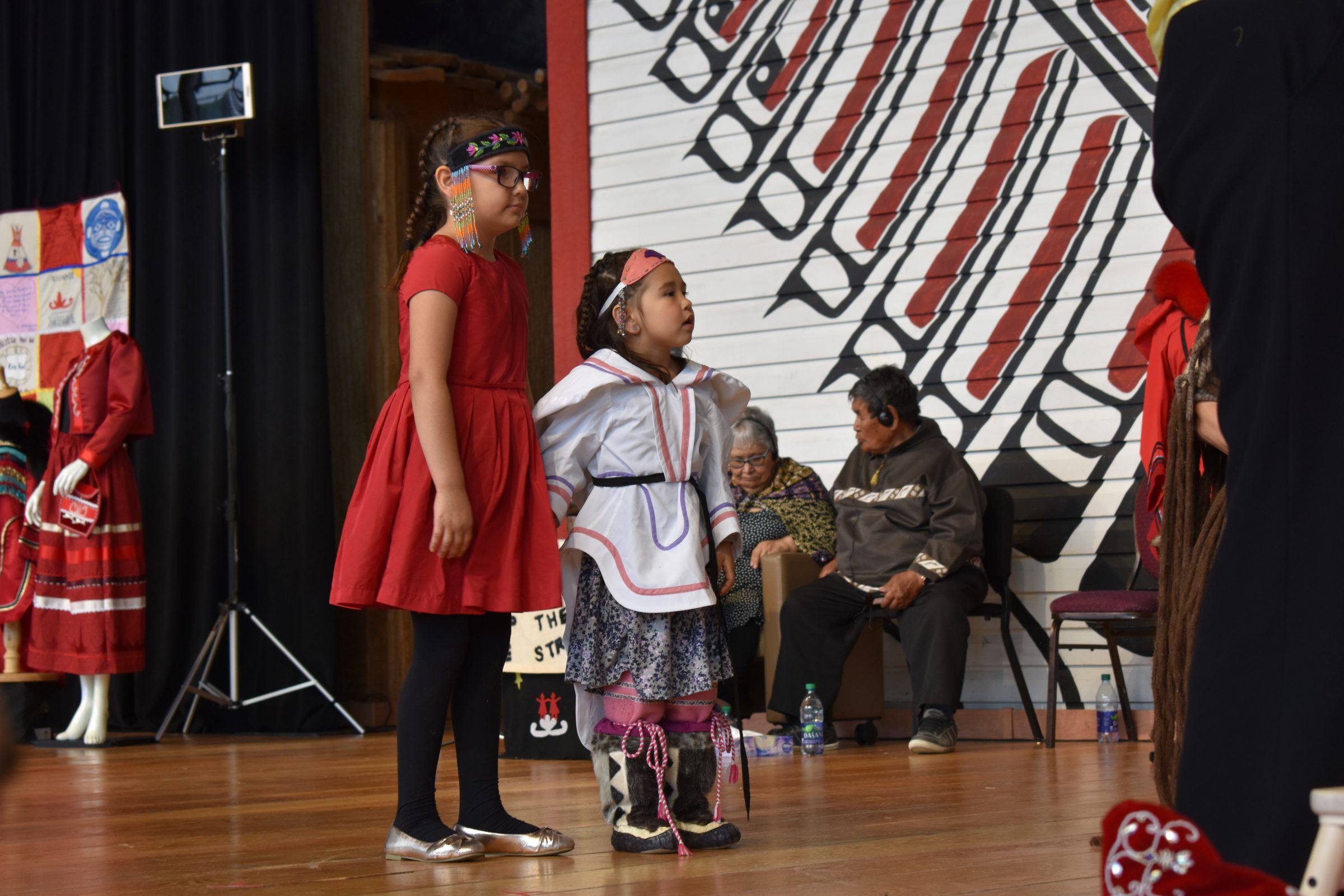 Two young Inuit girls watch the Tikinaagan (or cradleboard) ceremony, which prepared the final report of the National Inquiry into Missing and Murdered Indigenous Women and Girls so it could be passed to Prime Minister Justin Trudeau on Monday, June 3. The girls sat with Inuit elder Meeka Arnakak at the back of stage for the entirety of the closing ceremony, as the elder tended to a qulliq throughout the event. The children playing in the background brought a little lightness to the event, and for her final words a First Nations elder noted that the girls having such carefree fun was “the way it’s supposed to be” for young Indigenous children. (Photo by Kahlan Miron)