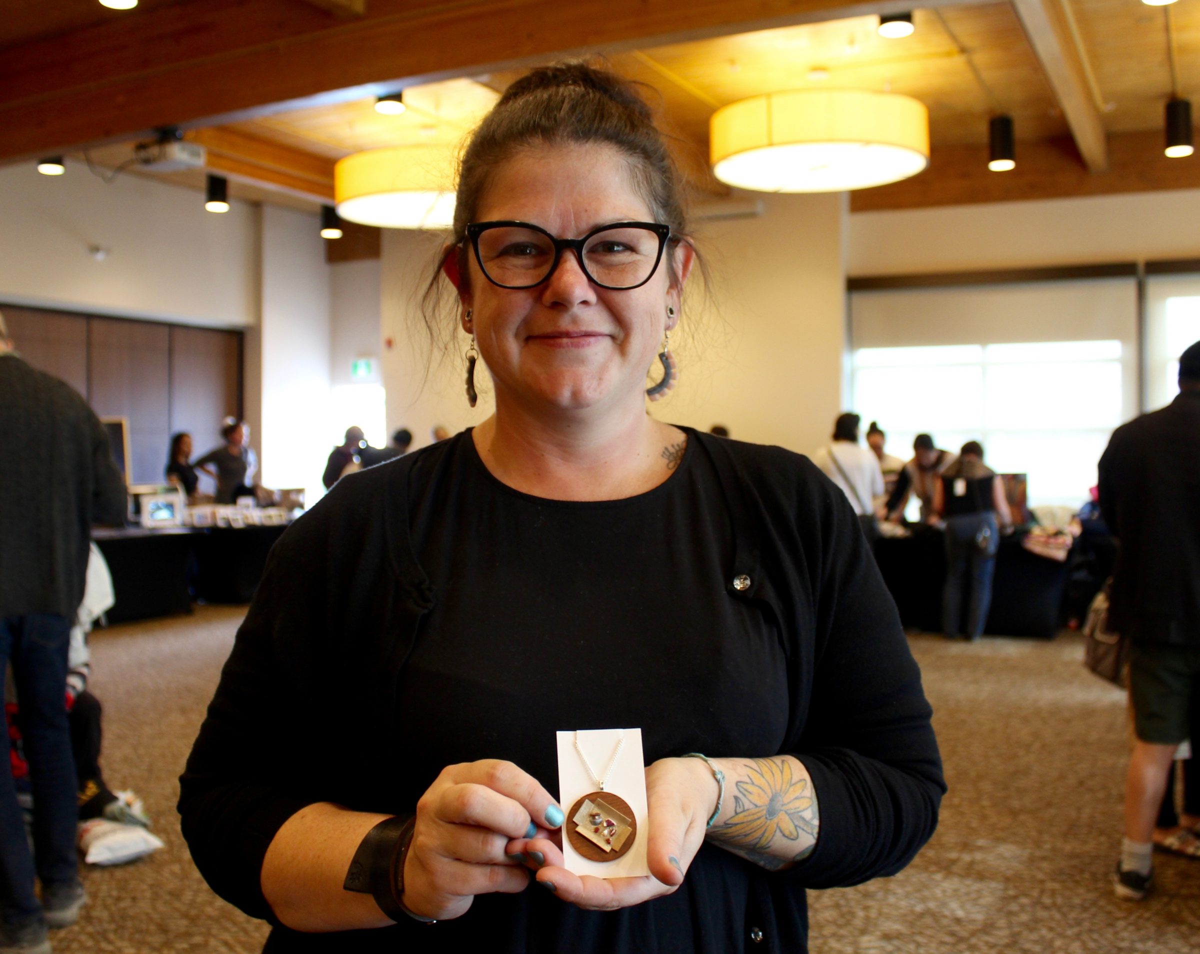 Iqaluit artist Erin Faulks shows off one of her pieces for sale at the craft fair held on Sunday, Aug. 25, at the Frobisher Inn as part of the Nunavut Arts and Crafts Association’s Nunavut Arts Festival in Iqaluit. Her necklaces feature tiny char, ulu, maktaaq and more on cardboard. The festival wrapped up over the weekend. (Photo by Emma Tranter)