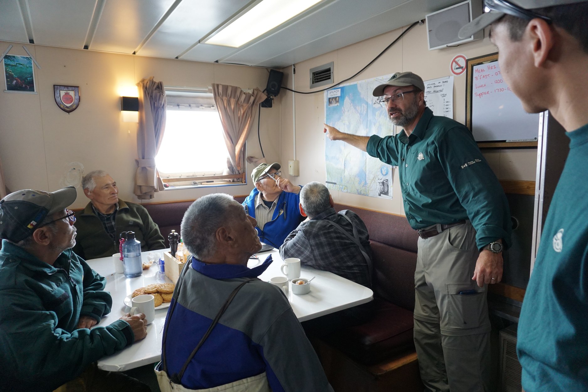 Elders from Gjoa Haven speak with Parks Canada’s manager of underwater archeology, Marc-André Bernier, aboard the Parks Canada vessel the David Thompson in early August. The elders, their family members and Inuit Guardians from Gjoa Haven came aboard the vessel as the Parks Canada crew prepared for dives to the wreck of HMS Terror, about 100 kilometres west of the community. From left: Joanasie Ukuqtunnuaq, Saul Qirniq, Tommy Tavalok (front), Ben Putuguq (corner), Jimmy Qirqqut, Marc-André Bernier, and underwater archeology team assistant Jonathan Puqiqnak (far right). (Photo courtesy of Parks Canada/Tamara Tarasoff)