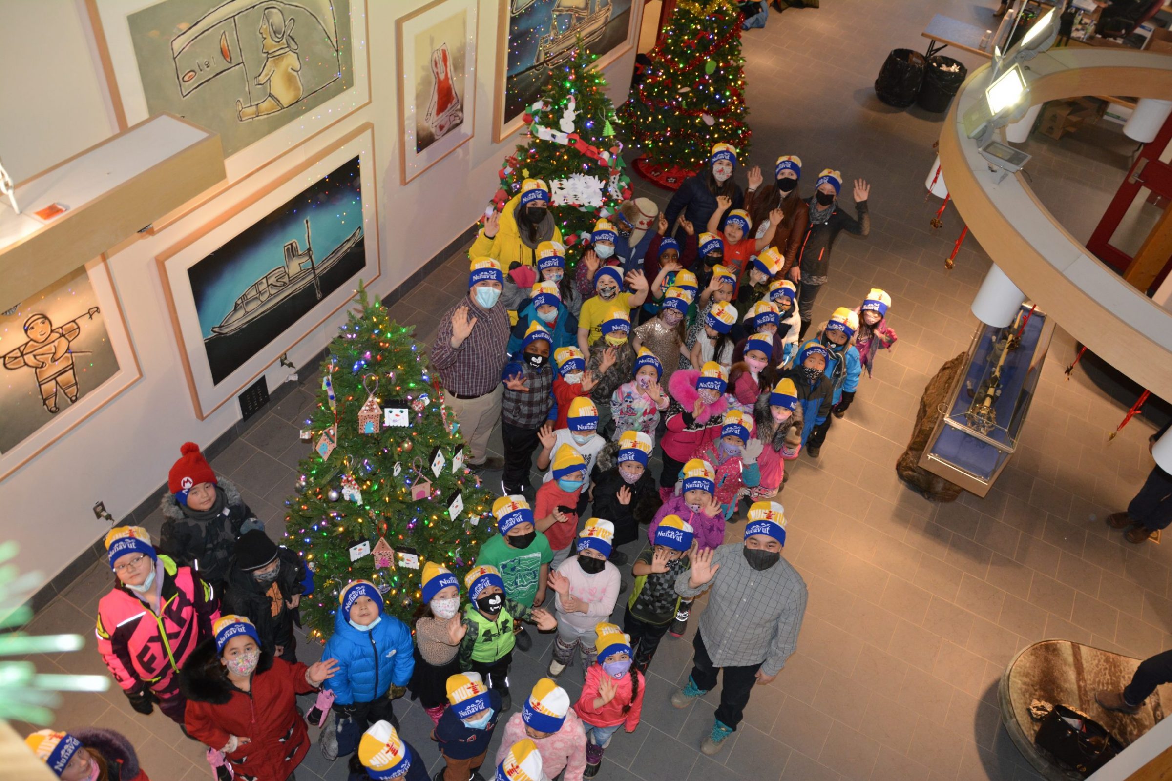 Elementary and middle school students from Iqaluit have been decorating Christmas trees in the lobby of the legislative building over the past few days. Here, Grade 1, 2 and 3 students from Nakasuk school are seen wearing toques they were given after lending a hand on Thursday. Premier P.J. Akeeagok also attended the first day of this year’s Christmas Lights Across Canada display at the legislature, which kicked off on Thursday. (Photo by Maggie Nooshoota)