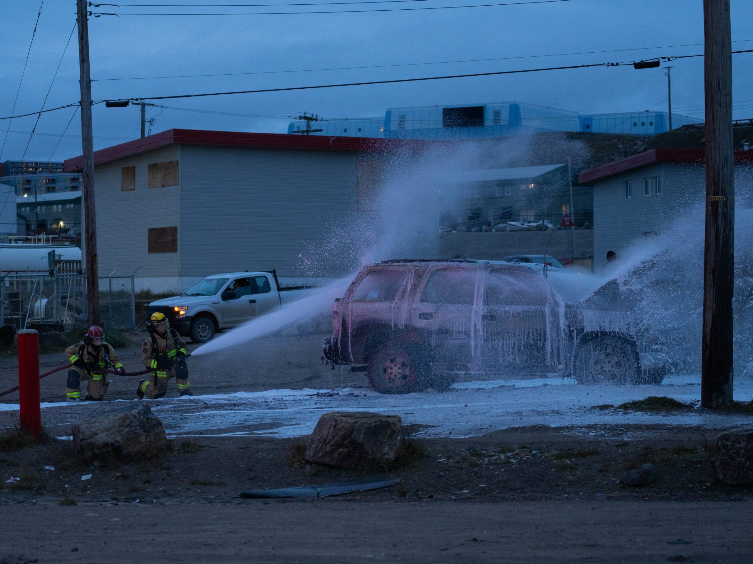 Firefighters hose down an SUV that caught fire near the Northwestel building in Iqaluit on Wednesday evening. According to city spokesperson Kent Driscoll, the fire was reported around 7:30 p.m. and firefighters declared it to be under control by 8:27 p.m. No one was injured and the RCMP is investigating the fire, he said. (Photo by Jason Sudlovenick)