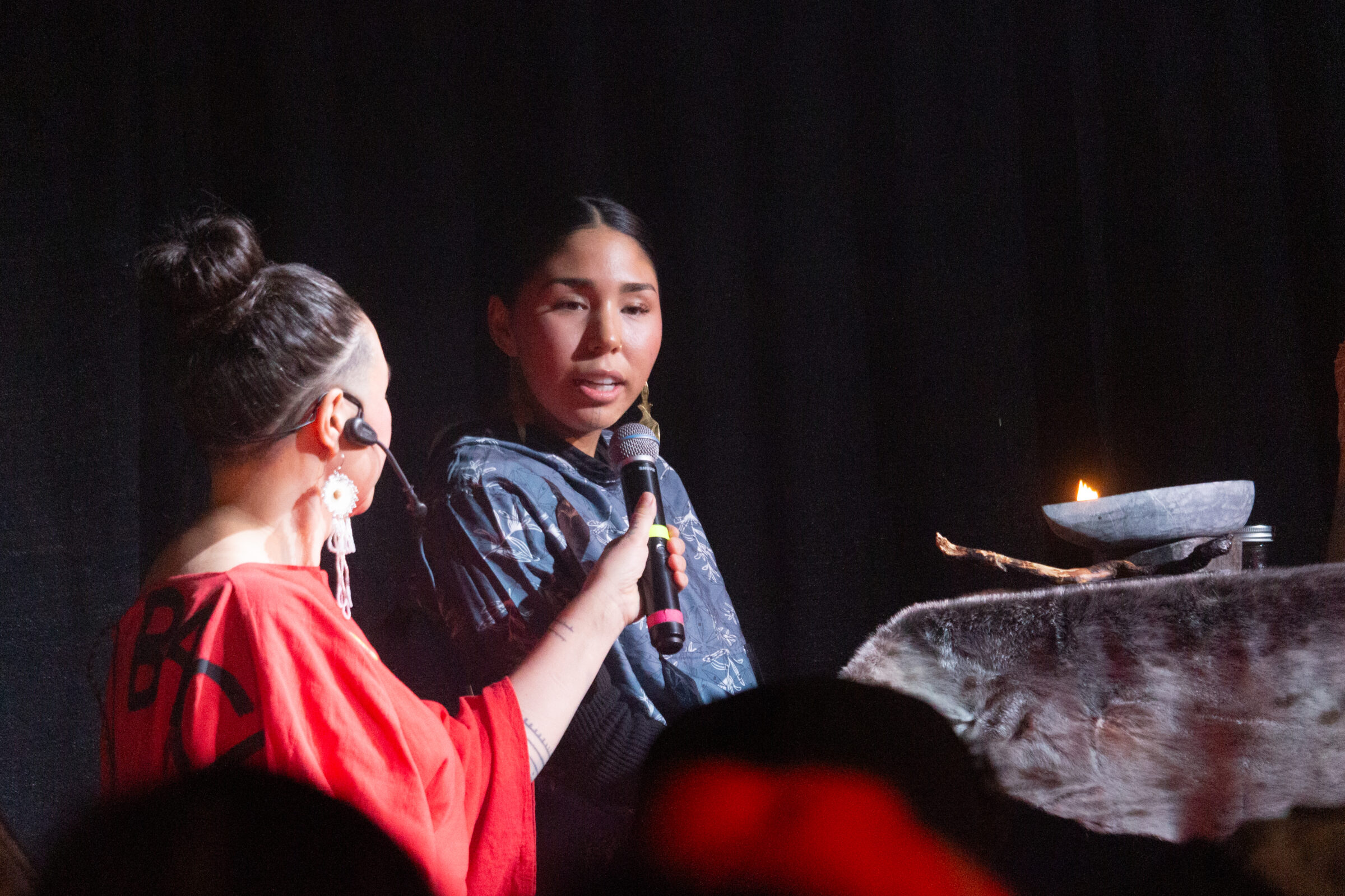 Laakkuluk Williamson, left, speaks to Naja Pearce who tends to a qulliq at the Pan-Arctic Vision music contest Saturday at the cadet hall in Iqaluit. Pearce kept the flame in the traditional oil lamp burning the entire event, which saw performers from nine Arctic regions vie for three prizes. (Photo by Jeff Pelletier)